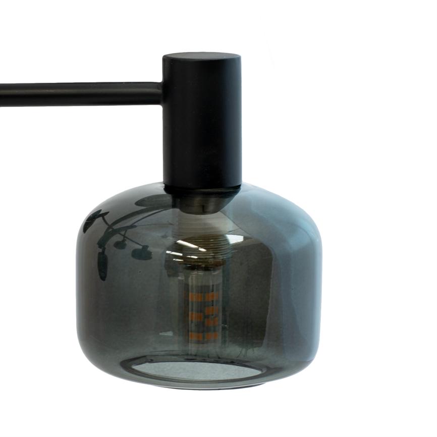 En røgfarvet glaspæreformet pendel hænger fra en sort metalarm; en LED-filamentpære er synlig gennem glasset, som reflekterer loftsbelysning og en plante mod en hvid baggrund.