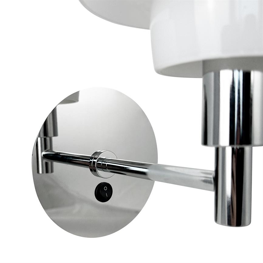 Kromvæglampe med rund vægplade og hvid skærm; armstykke strækker sig horisontalt fra pladen, blankpolerede metaloverflader reflekterer mod en ensartet hvid baggrund. 
 Tekst på afbryder: "O" og "I".