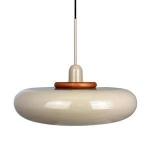 En rund, beige blank loftslampe hænger i en tynd stang og sort ledning; skærmen er donut-formet med træring øverst, minimalistisk hvid baggrund.