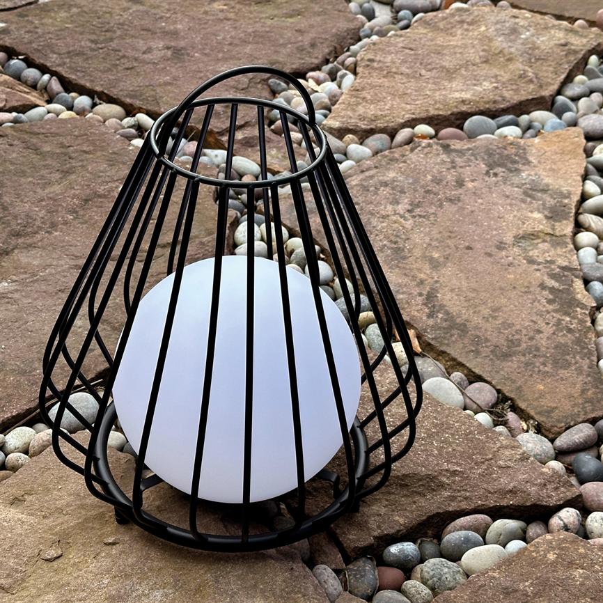 En hvid kugleformet lampe indkapslet i et sort metalbur står placeret på flade brune sten med små runde flodsten i fugerne.