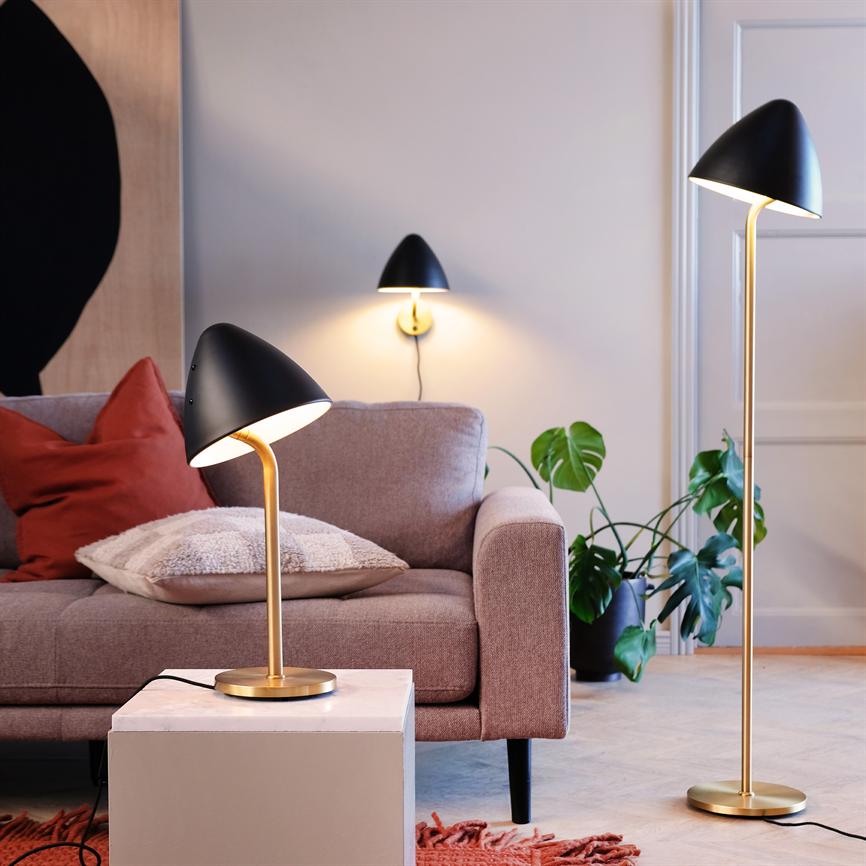 Tre moderne sorte og guldfarvede lamper kaster blødt, varmt lys over en lysrosa sofa i en hyggelig stue med puder, monstera-plante og et lille marmorbord.