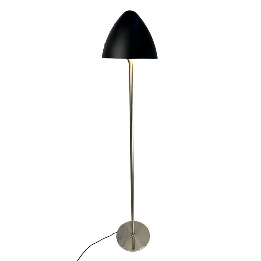 Gulvlampe står med sort kuppelformet skærm, tynd kromstang og rund metalfod; en sort ledning ligger ud fra foden mod en ensartet hvid baggrund.