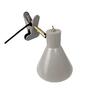 Klemme-lampe med grå, konisk skærm; gyldent leddetalje forbinder skærmen til en grå klemme, sort ledning fører væk; neutral hvid baggrund.