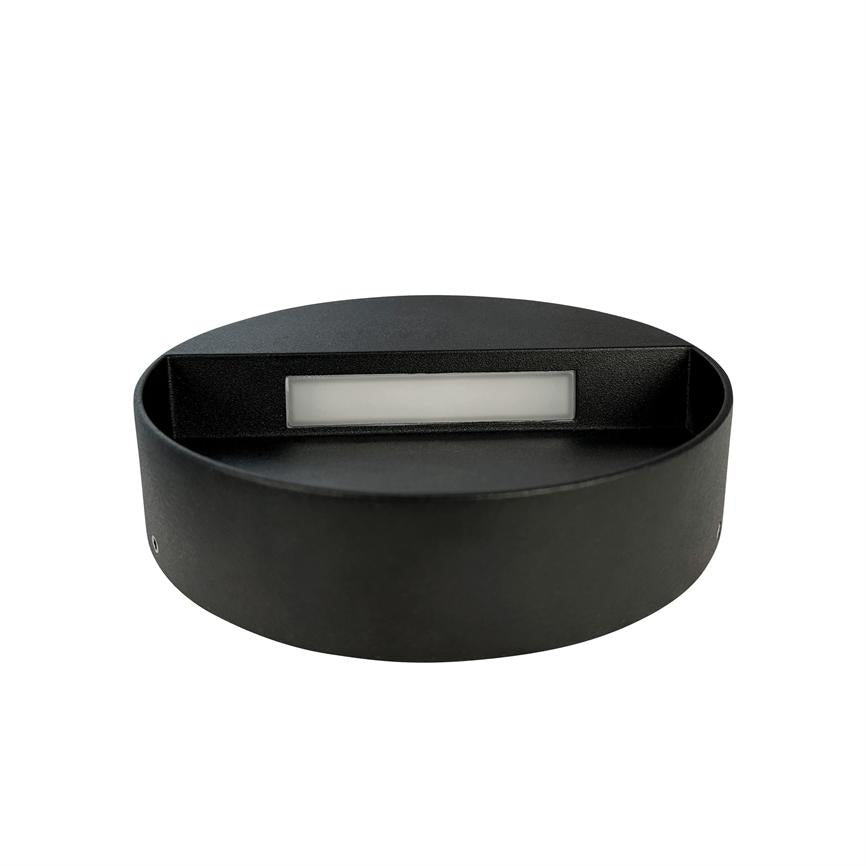 Sort, rund væglampe med en lav rektangulær lysåbning rettet nedad, placeret foran en ensartet hvid baggrund.