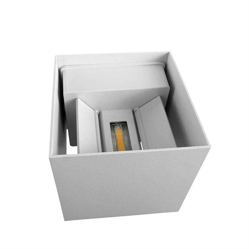 En hvid, kvadratisk lampeenhed rummer en central gul LED-modul; indvendige afskærmninger leder lyset, og en åben top viser en tekstureret kasse mod en neutral hvid baggrund.