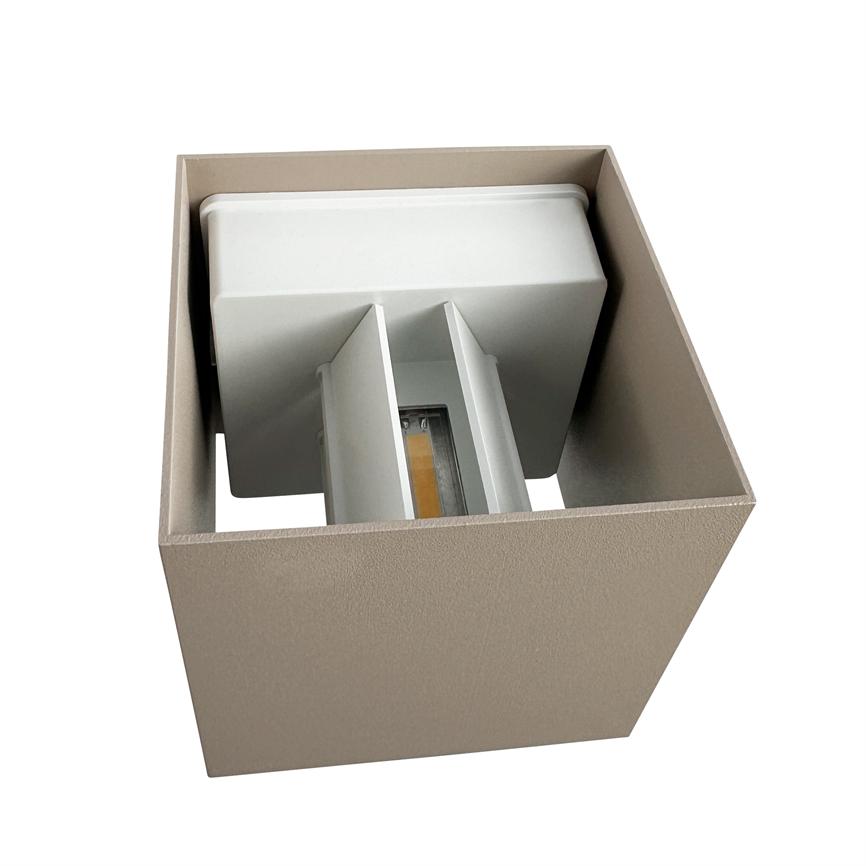 En firkantet, beige-metal væglampe rummer et indvendigt LED-modul placeret mellem to lamelskærme, pegende nedad; lampen ses isoleret mod en hvid baggrund.