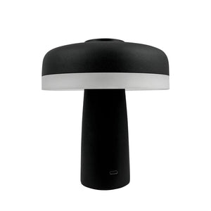 Bordlampe står med bred, rund skærm og cylindrisk fod; skærmens nederste kant er hvid, resten sort, mod en ensartet hvid baggrund.