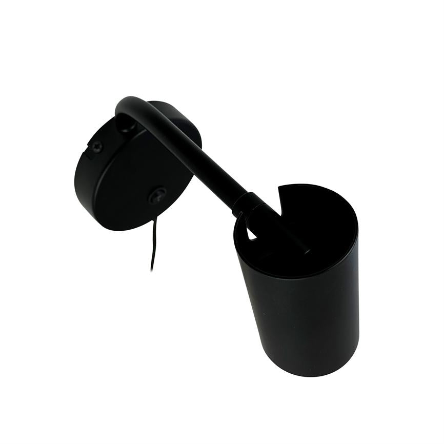 Vægmonteret sort spotlampe monteret på rund base, arm bøjet og pegende nedad, cylindrisk lampehus med kabel hængende, fotograferet mod hvid baggrund.