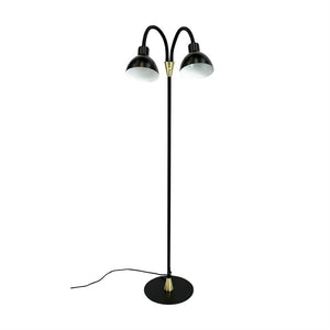 En sort gulvlampe med to buede skærme; armene bøjer udad og peger let nedad; står på rund sort fod med messingdetaljer og synlig sort ledning mod hvid baggrund.