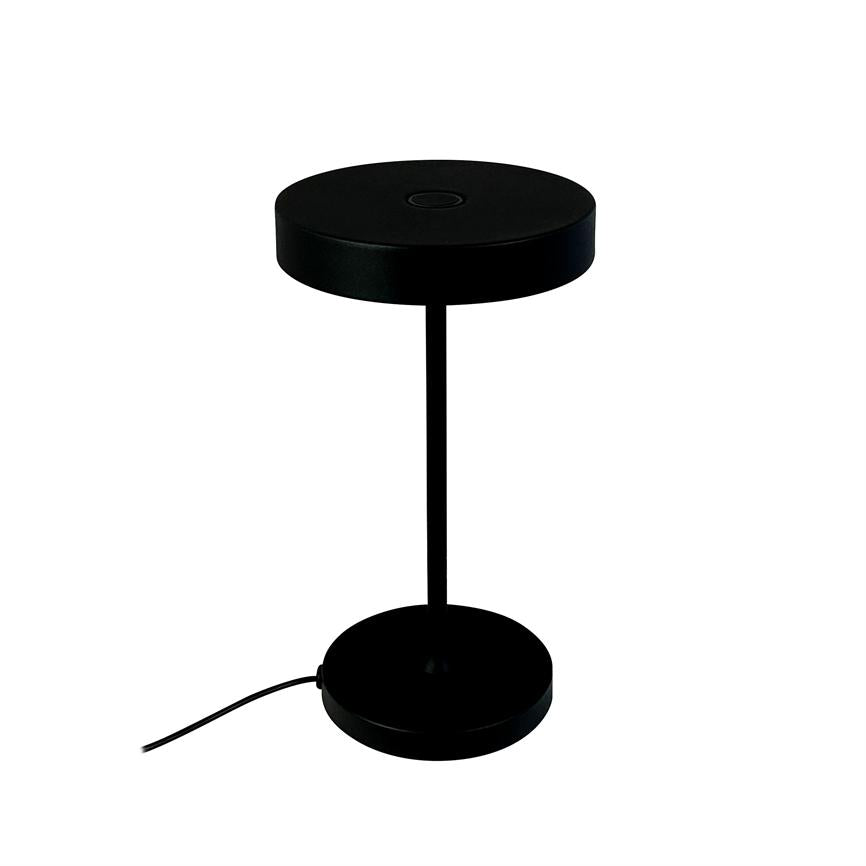 Sort cylindrisk bordlampe med rund top, tynd stang og cirkulær bund, synlig ledning og trykknap øverst, står oprejst på en ensartet hvid baggrund.