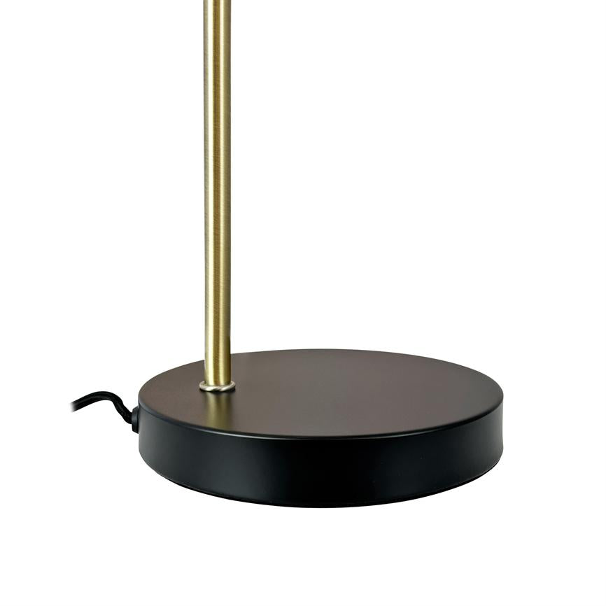 Lampens runde sorte fod understøtter en lodret, tynd messingstang; en sort netledning stikker ud mod venstre på en hvid baggrund.