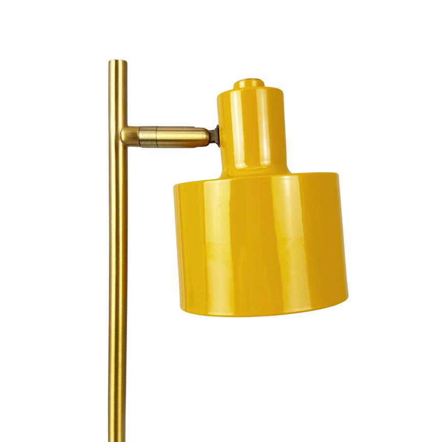 Gul lampeskærm monteret på en slank messingstang; cylinderformet skærm hælder let skråt, tilkoblet med et bevægeligt led mod en ensartet hvid baggrund.