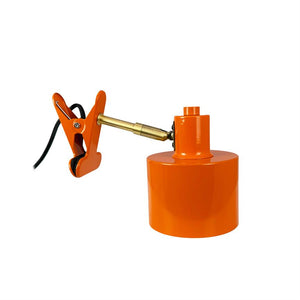 Klemme fastgør en justerbar messingarm til en orange cylindrisk lampebase med sort ledning på hvid baggrund.