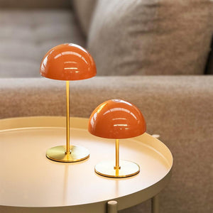 To små orange bordlamper står på et rundt bord, reflekterer lys og er placeret foran en beige sofa i en rolig, hyggelig stue.