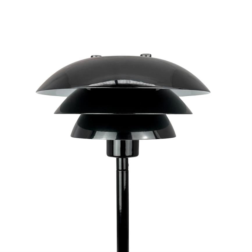 Sort bordlampe med tre lagdelte skærme står oprejst på en slank stang mod en ensartet hvid baggrund.