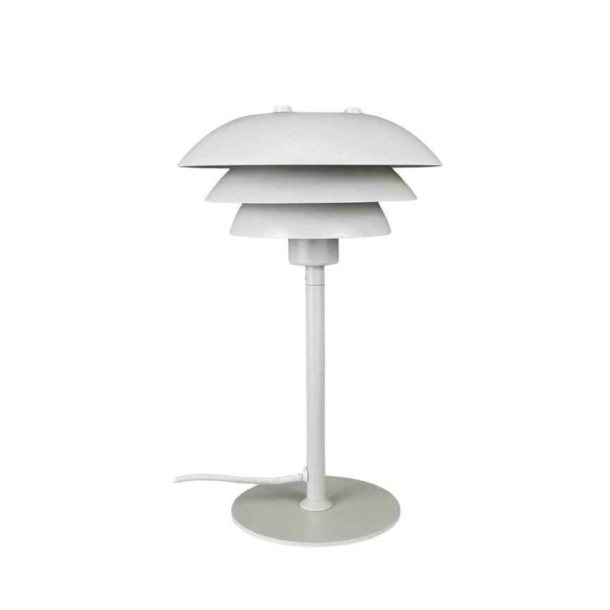 Hvid bordlampe med tre overlappende, skiveformede skærme, står på en slank stang og rund fod; tekstilledning ligger ved siden af, placeret mod ensartet hvid baggrund.