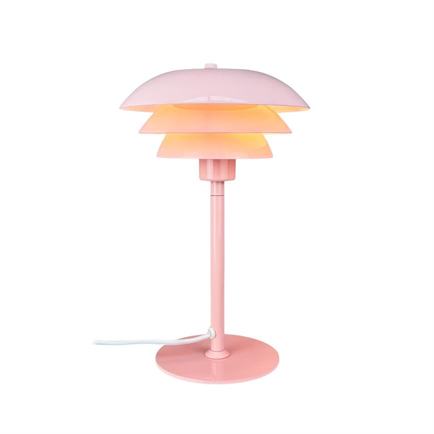Bordlampe i lyserød metal lyser med varmt, diffust lys gennem tre lag skærme, placeret på hvid baggrund med slank fod og hvid tekstilledning.